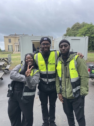 Rasheed with two colleagues in hi-vis outside the site office cabins at Brockwell Park