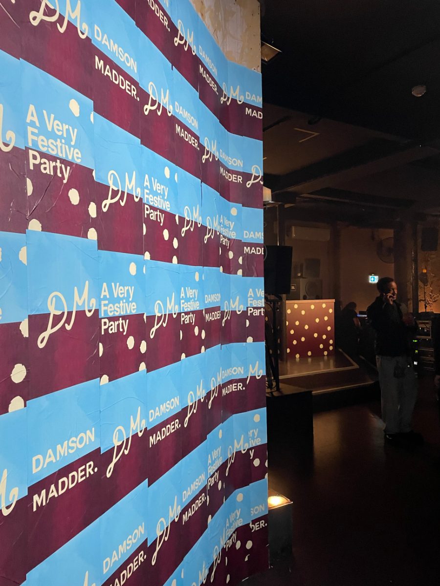 A wall pasted with Damson Madder: A Very Festive Party posters beside the venue floor
