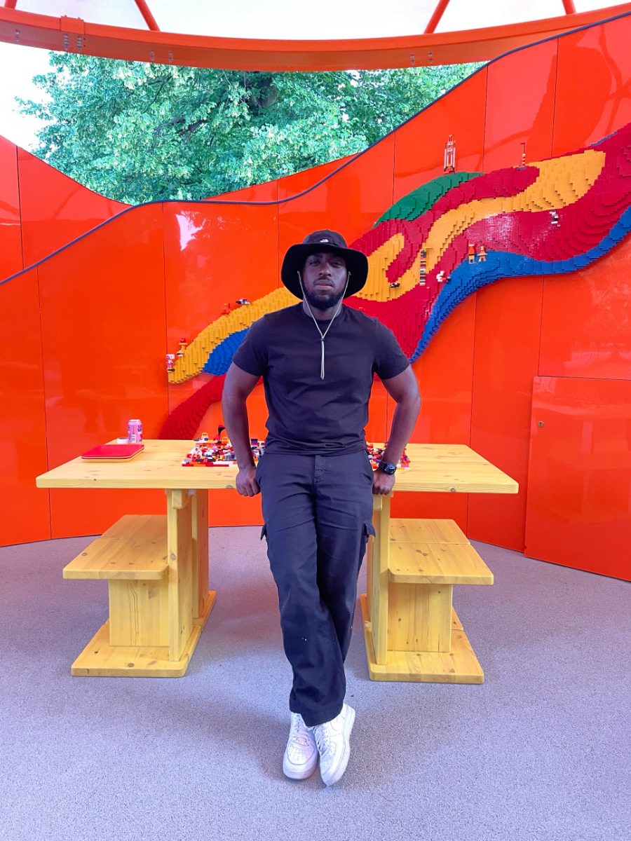 Rasheed inside the orange LEGO Play Pavilion at the Serpentine, in front of a LEGO brick river wall