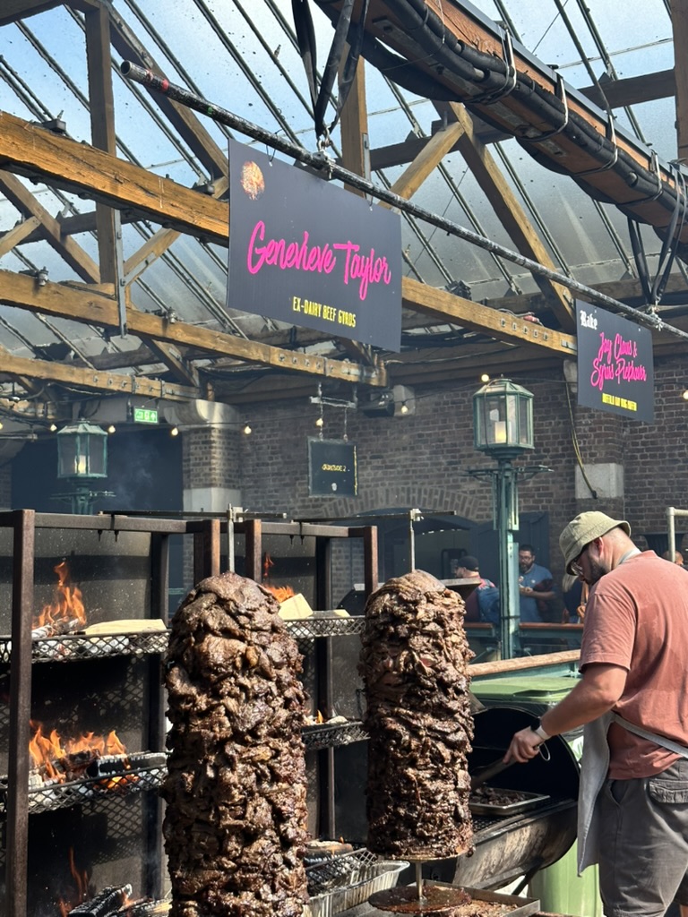 Live-fire cooking at Meatopia: two gyros turning beside open flames under the Tobacco Dock roof